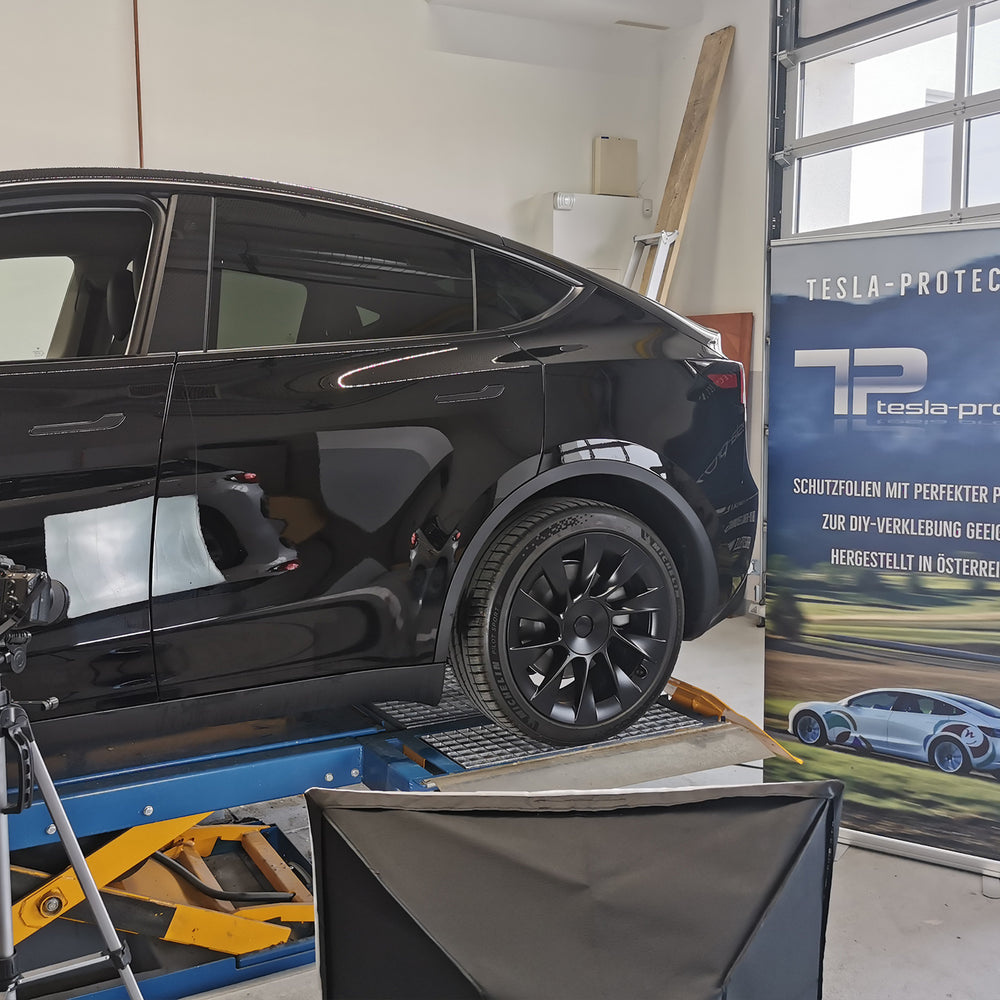 Zwarte Tesla Model Y op de hefbrug voor een banner van Tesla-Protect